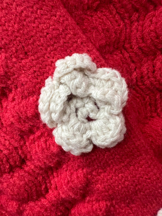 A close-up of a white crocheted flower detail attached to a bright red textured knit fabric.