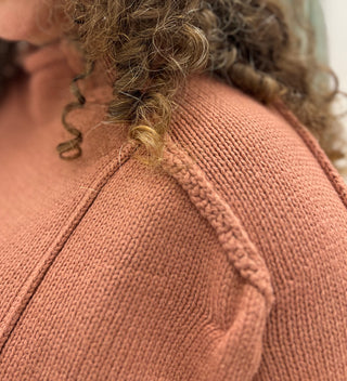 Close-up of a person wearing a textured knit sweater in a muted terracotta or dusty rose color, showing the shoulder seam and curly hair.