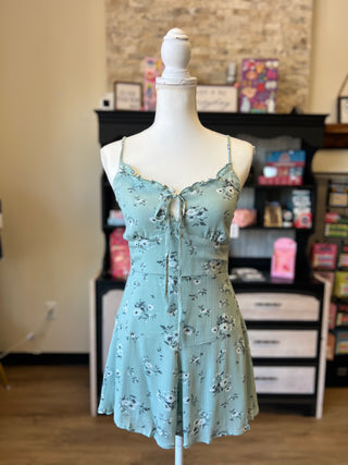 A light blue-green floral spaghetti-strap dress displayed on a white mannequin torso in a boutique setting.