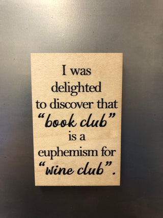 A rectangular wooden magnet with black printed text reading, "I was delighted to discover that 'book club' is a euphemism for 'wine club'" on a dark gray background.