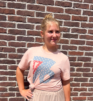 Person wearing a pink t-shirt with a graphic design in front of a brick wall