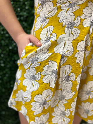 Close-up of a yellow dress or skirt with a large white floral print, shown on a person whose hand is visible holding the fabric.