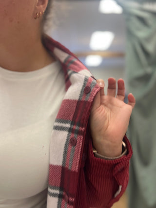 Close-up of a person wearing a red and white plaid button-up shirt over a white top, with their hand lifting the plaid collar.