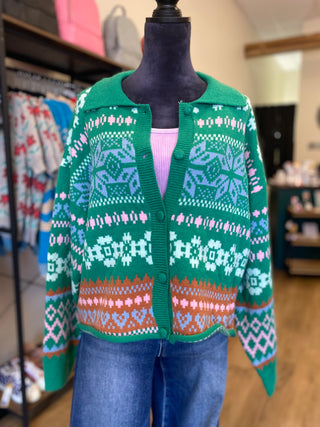 A green knit cardigan sweater with a multicolor Fair Isle pattern, displayed on a black mannequin torso inside a clothing store.