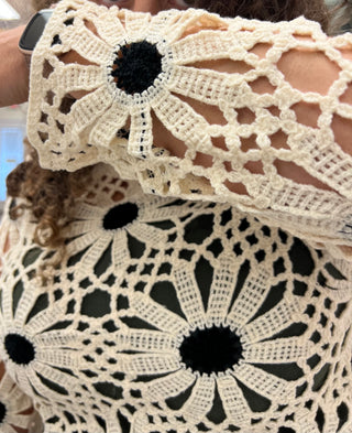 Close-up of a person wearing a cream crocheted top with large sunflower-like motifs and black centers, with part of a matching crocheted sleeve or accessory visible.