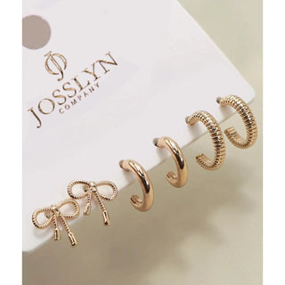 Four gold-toned hoop earrings displayed on a white Josslyn Company card, including a bow-shaped hoop, a smooth curved hoop, and two textured spiral hoop styles.