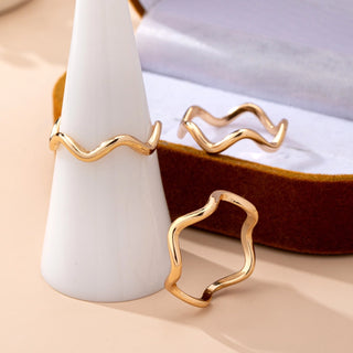 Gold open ring with wavy design on a beige surface