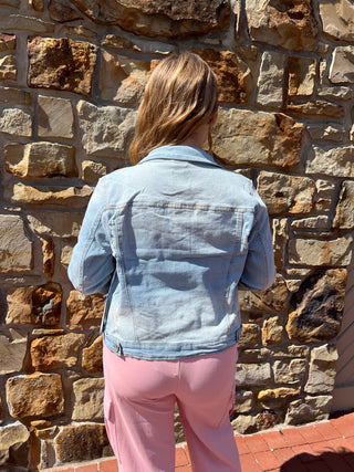 A person viewed from above wearing a light blue denim jacket and pink pants, standing on a stone wall outdoors.