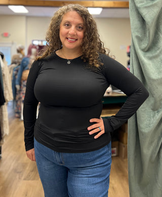 A woman with curly brown hair wearing a fitted black long-sleeve top and blue jeans, standing in a clothing store.