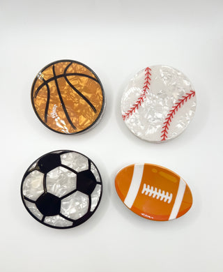 Four oval hair clips sports designs, including a basketball, baseball, soccer, and football pattern, arranged on a plain white background.
