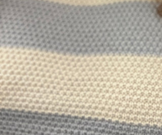 A close-up of a woven textile with horizontal stripes in light blue-gray and warm cream, showing a textured knit or boucle pattern.