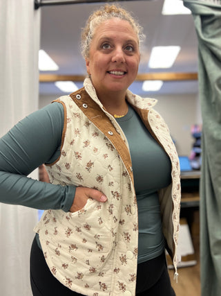 A woman wearing a cream quilted vest with a brown floral pattern and tan corduroy collar, layered over a slate green long-sleeve top.