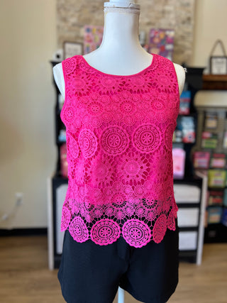 A sleeveless bright pink crochet lace top displayed on a white mannequin torso, paired with black shorts, in an indoor boutique setting.