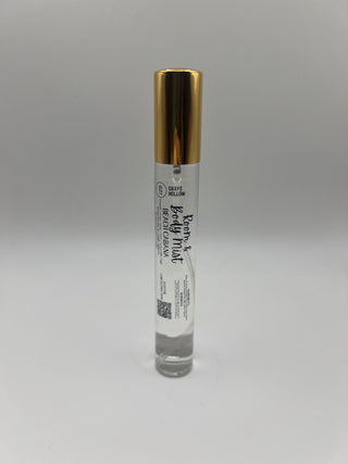 A small clear glass rollerball bottle of Room & Body Mist in Beach Carama, featuring a shiny gold cap and a white label, shown on a plain light gray background.