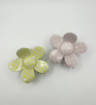 Two flower-shaped hair claw clips on a plain white background. One clip is light green with a yellow checkerboard pattern, and the other is light pink with a peach checkerboard pattern.
