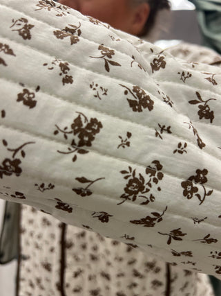 A close-up of a quilted white fabric with a brown floral pattern, held up to show the texture and print detail.
