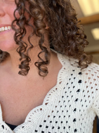 Close-up of a person with dark brown curly hair wearing a white open-knit crochet top.