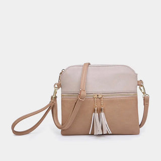 A two-tone crossbody handbag in light beige and dusty pink faux leather, featuring a front zip pocket with dual white tassels and a matching shoulder strap, set against a plain light gray background.