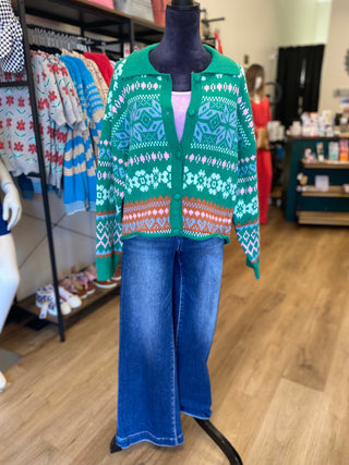 A green Fair Isle pattern knit cardigan sweater displayed on a black mannequin torso, paired with blue jeans, in a retail store setting.