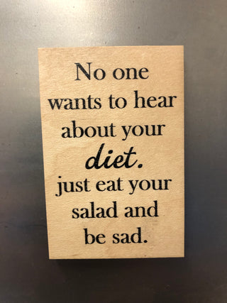 A rectangular wooden magnet with black printed text that reads, 'No one wants to hear about your diet. just eat your salad and be sad.