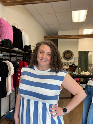A woman with curly brown hair wearing a blue and white striped top, smiling and posing in a retail store environment.