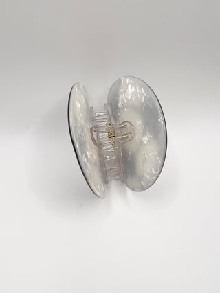 A clear acrylic hair claw clip with a subtle white marble pattern, shown from a side profile view on a light gray background.