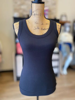 A sleeveless ribbed scoop-neck tank top in dark navy blue displayed on a wooden dress form mannequin, with a softly blurred boutique interior in the background.