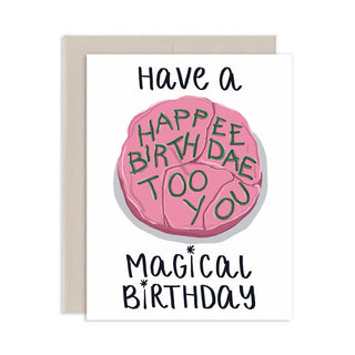 A white greeting card with a light beige envelope behind it, featuring a pink brain illustration with the words 'HAPPEN BIRTHDAE TOO YOU' in green and black text reading 'Have a Magical Birthday'.