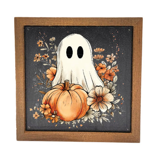 A square framed art print featuring a white ghost with black eyes behind a orange pumpkin and autumn flowers on a dark background, set in a rustic brown wooden frame.