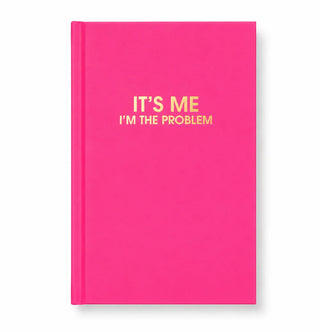 A bright pink hardcover notebook with gold foil text on the front reading 'IT'S ME I'M THE PROBLEM' against a clean white background.