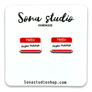 Two small name-tag style earrings displayed on a white backing card. Each tag has a red header with white 'Hello' text and a white body reading 'Regina Phalange.