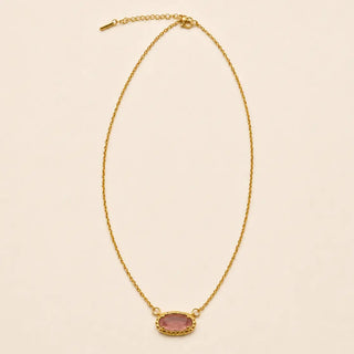 A delicate gold chain necklace featuring an oval pink gemstone pendant with a textured gold border, displayed on a solid light beige background.