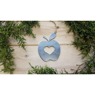 Decorative metal apple with heart cutout on a wooden background with greenery