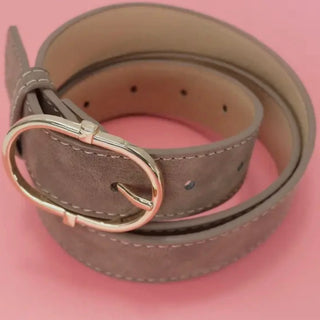 A taupe-brown suede belt with a silver-tone metal buckle, neatly coiled on a solid pink background.