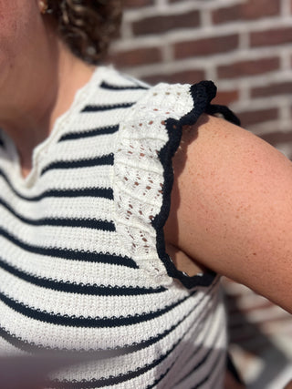 Person wearing a striped shirt with a textured sleeve against a brick wall.