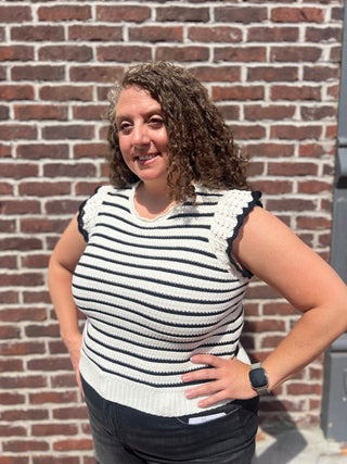 Woman wearing a black and white striped sleeveless top with lace details against a brick wall.