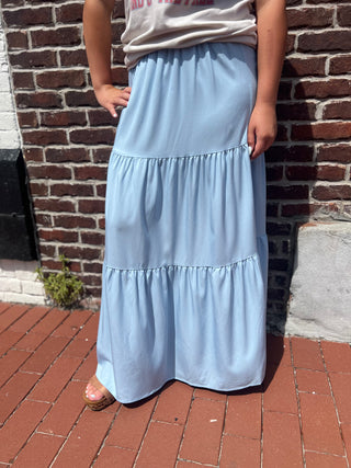 Person wearing a light blue tiered skirt standing against a brick wall.