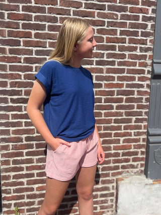 Person wearing a blue shirt and red and white striped shorts standing against a brick wall.