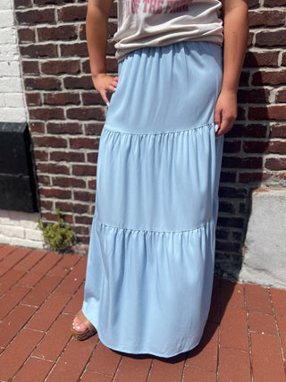 Person wearing a light blue tiered skirt standing against a brick wall.