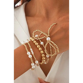 Gold and pearl beaded bracelets on a wrist with a white background