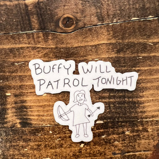 A die-cut sticker with the text 'BUFFY WILL PATROL TONIGHT' and a simple line drawing of a girl holding a bow, placed on a rustic brown wooden surface.