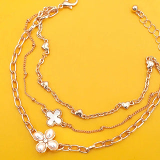A layered silver-tone chain bracelet with a flower and heart charms, displayed on a bright yellow background.