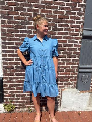 Woman in a blue dress standing against a brick wall.