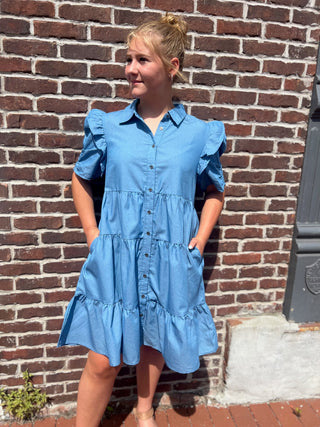 Woman wearing a blue dress standing against a brick wall.