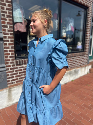 Woman wearing a blue dress standing on a sidewalk with a brick building in the background