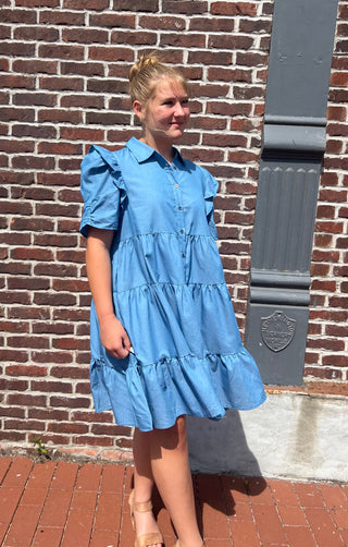 Woman wearing a blue dress standing against a brick wall.