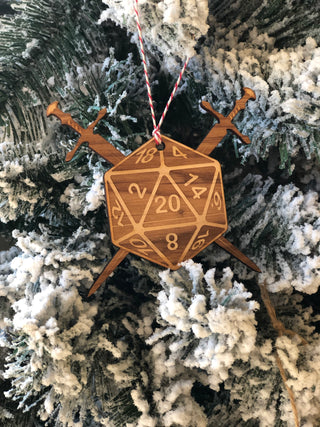 A wooden 20-sided die ornament with crossed swords and a red-and-white string, hanging on a frosted Christmas tree.