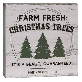 A square decorative wooden sign with a distressed white wood-grain finish. The sign features black text reading 'FARM FRESH CHRISTMAS TREES' and 'IT'S A BEAUT, GUARANTEED!' along with three dark green pine tree silhouettes.