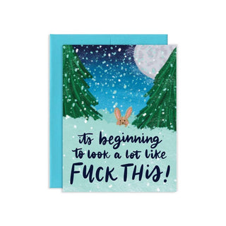 A greeting card with a snowy winter forest illustration and a small bunny, paired with a light blue envelope. The card reads, 'it's beginning to look a lot like FUCK THIS!'.