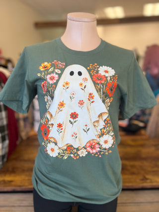A sage green short-sleeve t-shirt displayed on a mannequin torso in a retail store. The shirt features a large graphic of a white ghost decorated with orange, red, pink, and white wildflowers.